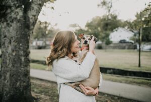 A joyful woman hugs her pet dog outdoors in a sunny park setting, showcasing affection and togetherness.